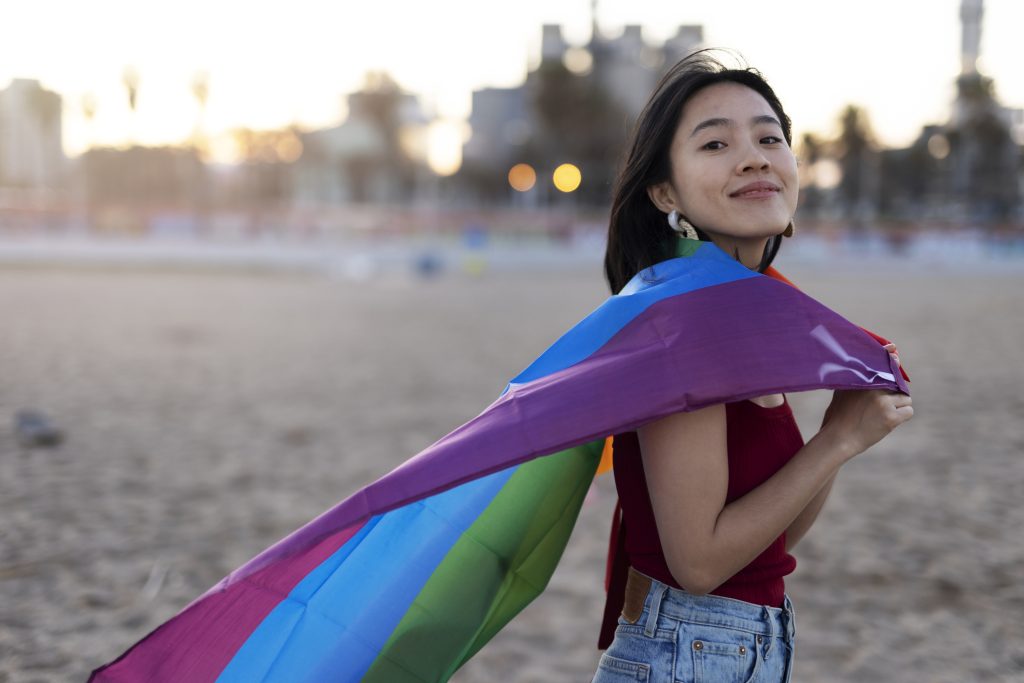 Happy girl with a pride flag at the beach.